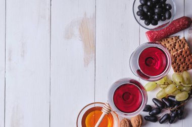 Romantik bir akşam yemeği için lezzetli ürünler. Sosis, fındık, meyve, zeytin, ekmek, üzüm, şarap ve bal eski beyaz ahşap bir masada. Üst görünüm.