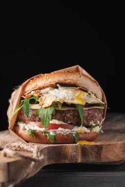 close up of mouth-watering burger with grilled beef patty and fresh vegetables. Tasty american cheeseburger on wooden board. 