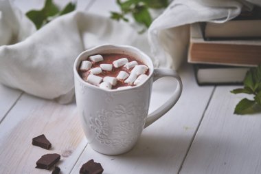Bir kupa naneli sıcak çikolata ve beyaz ahşap bir masada lokum. Sonbahar akşamı: kitaplar, çikolata ve sıcak bir içecek..