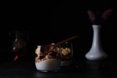 Akşam yemeğinde yoğurtlu müsli ve beyaz vazoda çiçekler. Siyah arkaplan.