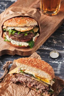 close up of mouth-watering burger with grilled beef patty and fresh vegetables. Tasty american cheeseburger on wooden board. 