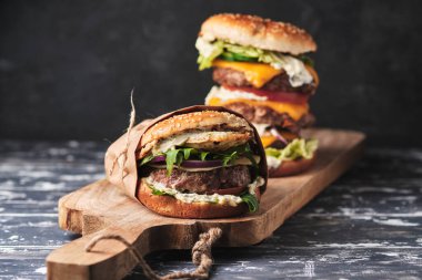 close up of mouth-watering burger with grilled beef patty and fresh vegetables. Tasty american cheeseburger on wooden board. 