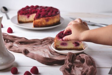Sabah kahvaltısı, espresso ve ahudududulu peynirli kek. Bir çocuk bir parça tatlıdan ahududu yer. Beyaz ahşap masada kahvaltı..