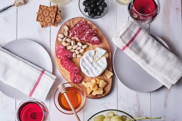 İki kişilik romantik bir yemek. Peynir ve sosis lezzetleri, fındık, meyve, zeytin, ekmek, üzüm, şarap ve bal eski beyaz ahşap bir masada. Üst görünüm.
