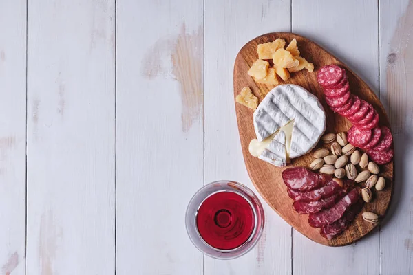 Cheese and sausage delicacies, nuts, a glass of wine on an old white wooden table. Food and wine for a romantic dinner. Top view.