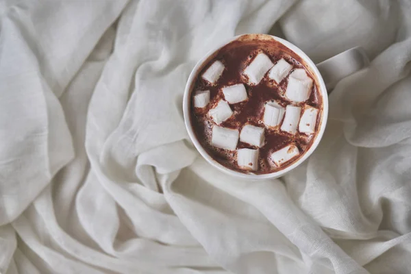 Mug of hot chocolate with marshmallows on a light textile background. White mug of hot drink close-up. Top view.