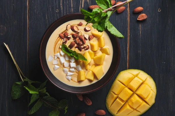 Tropical smoothie bowl with banana, mango, coconut and nuts. Refreshing dessert with mint on an old wooden table