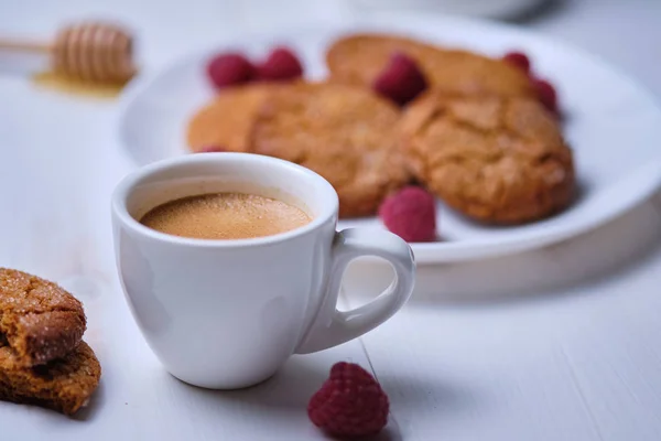 Morning espresso with honey cookies and raspberries. Breakfast on the white kitchen table.