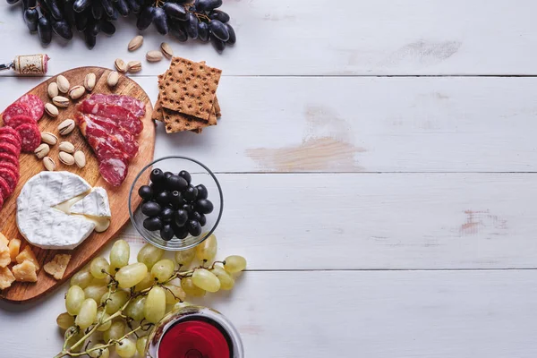 Delicious products for a romantic dinner. Cheese and sausage delicacies, nuts, fruits, olives, bread, grapes, wine and honey on an old white wooden table. View from above.