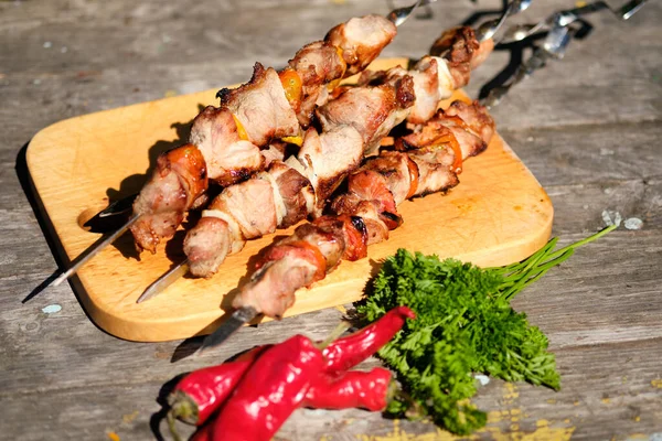 Ahşap bir masada taze pişirilmiş barbekü ve sebzeler. Doğada yaz yemeği. Lezzetli et yemeği ateşte pişmiş..