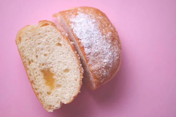 Close-up of a sliced stuffed donut decorated with icing sugar on a pink paper background. Top view.