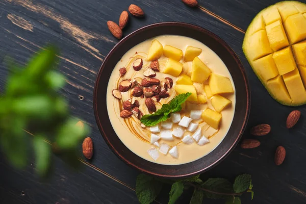 Muz, mango, hindistan cevizi ve fındıklı tropik meyve suyu kasesi. Tatlıyı eski ahşap bir masada nane şekeriyle tazeliyorum.