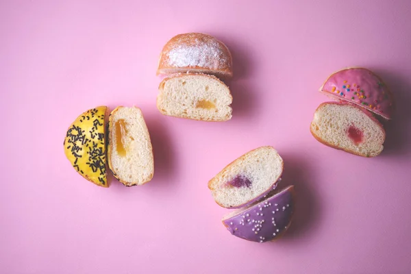 Close-up of sliced stuffed donuts decorated with colored glaze on a pink paper background. Top view.