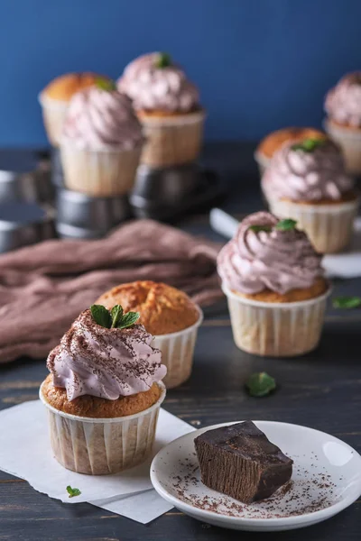 The process of making holiday cupcakes with pink cream. The dessert is decorated with mint leaves and chocolate chips. Background color classic blue.