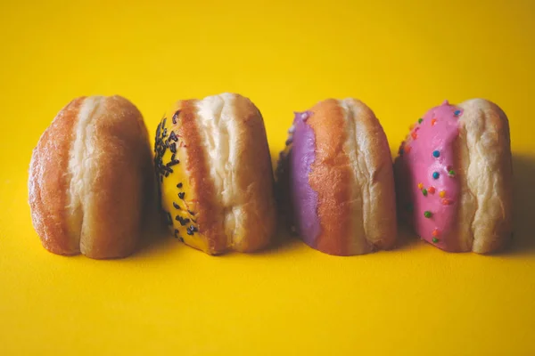 Close-up of sliced stuffed donuts decorated with colored glaze on a yellow paper background.