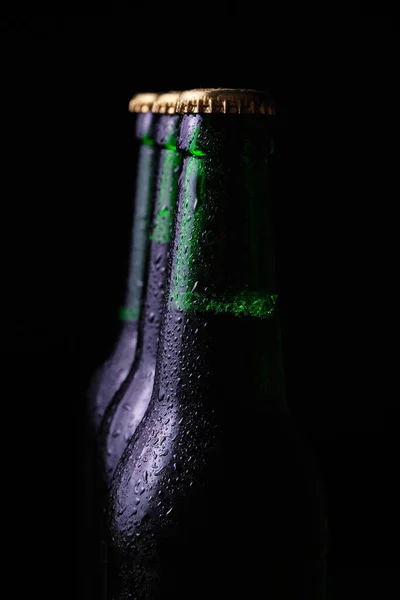 Three misted bottles of cold beer on a black background.