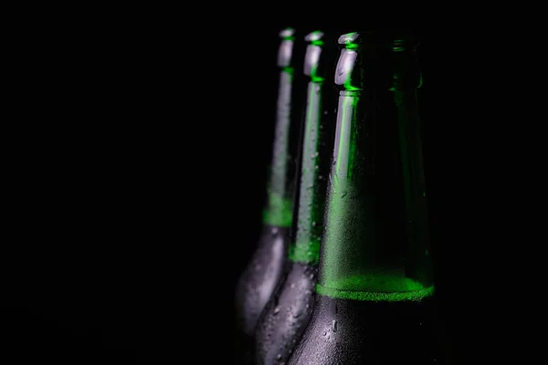 Three misted open bottles of cold beer on a black background.