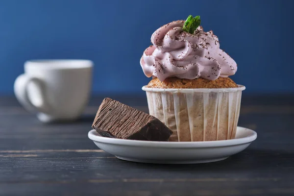 Festive cupcake with pink cream on a plate. The dessert is decorated with mint leaves and chocolate chips. Background color classic blue.