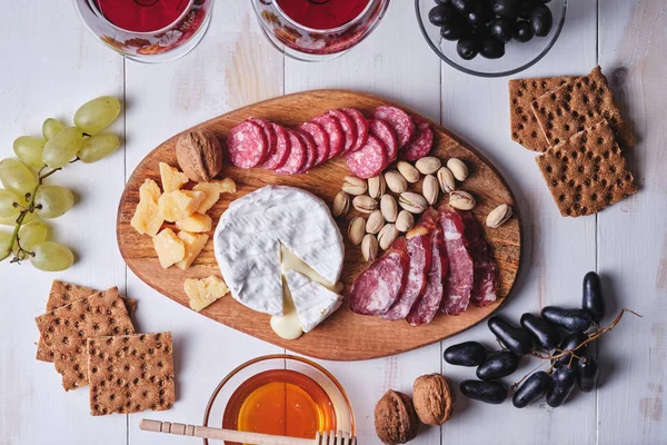 Romantik bir akşam yemeği için lezzetli ürünler. Peynir ve sosis lezzetleri, fındık, meyve, zeytin, ekmek, üzüm, şarap ve bal eski beyaz ahşap bir masada. Üst görünüm.