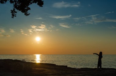 Sahilde durup güneşi gösteren kız.
