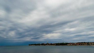 Gökyüzünde fırtınalı bulutların dalgalandığı bir yarımadada yer alan kilise kulesiyle Hırvat köyü San Lorenzo 'nun zaman aşımı.