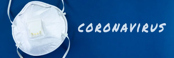 Face mask on blue background corona virus written in white colour in conceptual image of public health threatening virus.