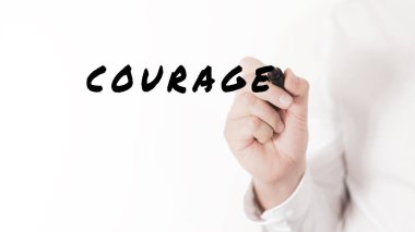 Bir iş adamının eli, cesaret ve kararlılığın kavramsal görüntüsüyle siyah kalemle bir kelime yazıyor.