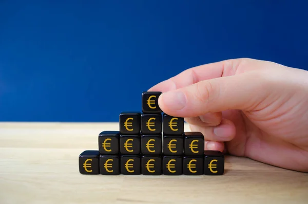 İşadamı, maddi büyümenin kavramsal görüntüsünde piramit şeklinde altın euro işaretleriyle siyah zarları birleştiriyor