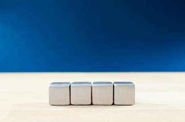 Sıraya dizilmiş dört boş gümüş blok koyu mavi arka planlı bir meşe ağacından yapılmış..