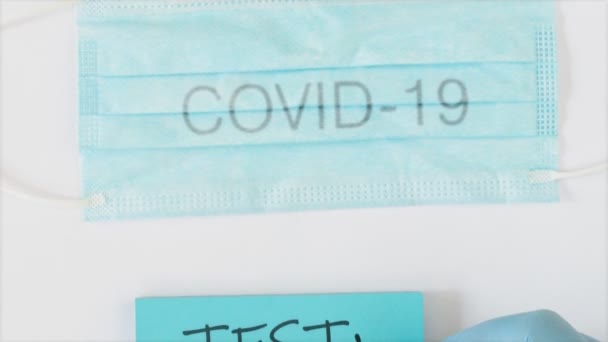 Surgical protective mask with Covid-19 sign and a hand in glove writting test results on blue paper — Stock Video