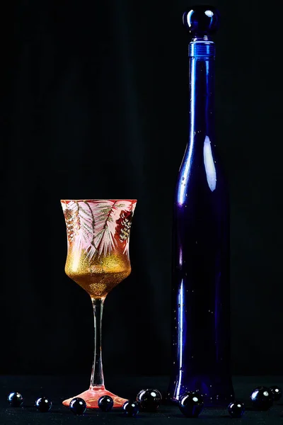 Elegant blue bottle of expensive wine gift with drops of water with wineglass  on a black background isolated in detail in macro with a glimmer of light