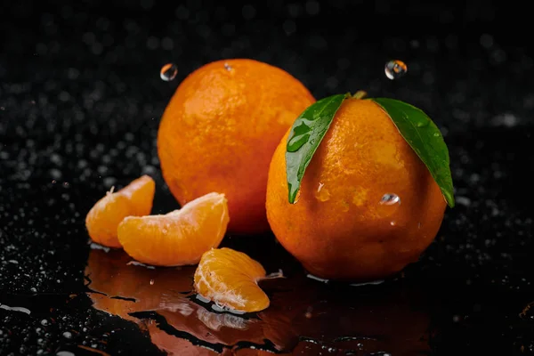 Siyah zemin üzerinde su damlaları olan mandalinalar. Yeni 