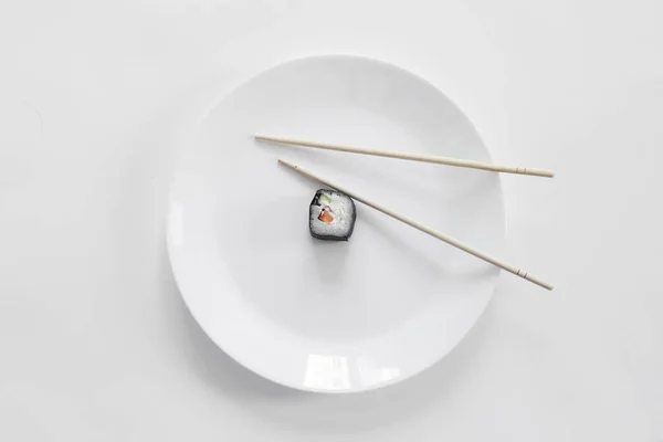 Suşi beyaz tabakta çubuklarla yuvarlanıyor.