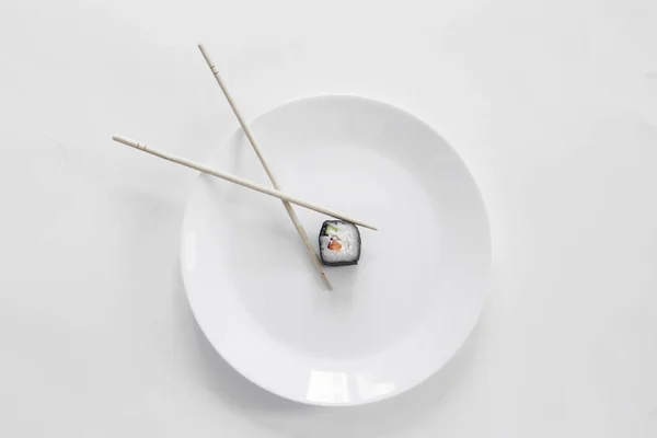 Gri arka planda çubuklarla beyaz bir tabakta suşi.