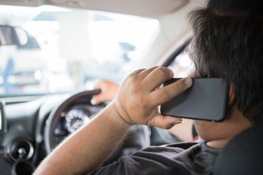 Adam araba sürerken cep telefonundan konuşuyor.