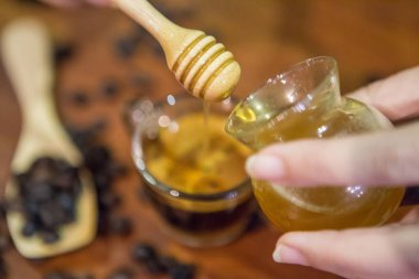 Kadın eli bir fincan kahveye bal dolduruyor.