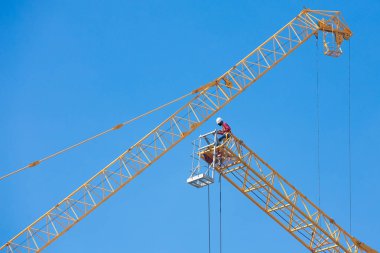 Mavi gökyüzünde büyük bir inşaat vinci üzerinde çalışanlar