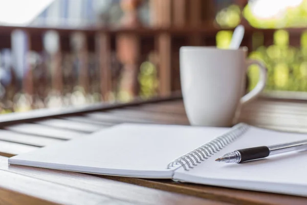 Kalem, defter ve kahve fincanının seçmeli odak noktası ahşap masa üzerinde sıcak ışık ve kopyalama alanı