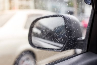Bulanık arkaplanda, arabanın yan aynasındaki yağmur damlalarının seçici odağı