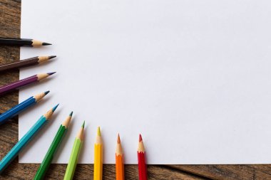 Ahşap arka planda renkli kalem ve beyaz kağıt