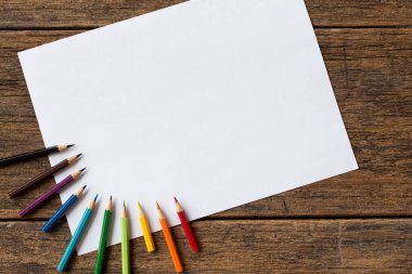 Ahşap arka planda renkli kalem ve beyaz kağıt