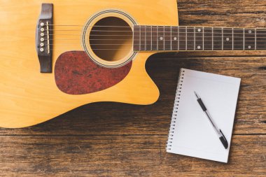 Akustik gitarın, Not Defteri kağıdının ve tahta zemin üzerindeki kalemin üst görünümü ve boşluğu kopyala