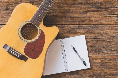 Akustik gitarın, Not Defteri kağıdının ve tahta zemin üzerindeki kalemin üst görünümü ve boşluğu kopyala