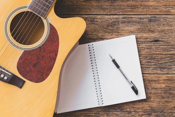 Akustik gitarın, Not Defteri kağıdının ve tahta zemin üzerindeki kalemin üst görünümü ve boşluğu kopyala