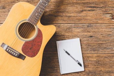 Akustik gitarın, Not Defteri kağıdının ve tahta zemin üzerindeki kalemin üst görünümü ve boşluğu kopyala