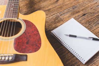 Akustik gitarın seçici odak noktası, tahta arkaplan üzerine defter kağıdı ve kalem ve boşluk kopyala
