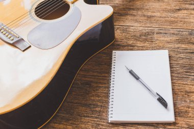 Akustik gitarın seçici odak noktası, tahta arkaplan üzerine defter kağıdı ve kalem ve boşluk kopyala