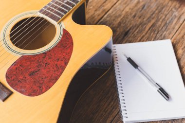 Akustik gitarın seçici odak noktası, tahta arkaplan üzerine defter kağıdı ve kalem ve boşluk kopyala