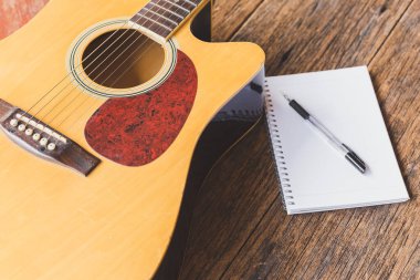 Akustik gitarın seçici odak noktası, tahta arkaplan üzerine defter kağıdı ve kalem ve boşluk kopyala