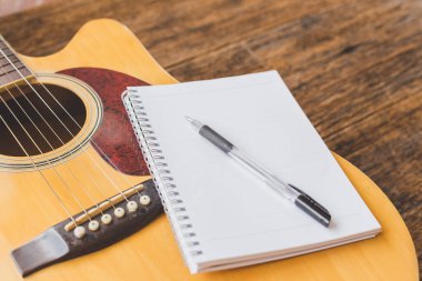 Akustik gitarın seçici odak noktası, tahta arkaplan üzerine defter kağıdı ve kalem ve boşluk kopyala